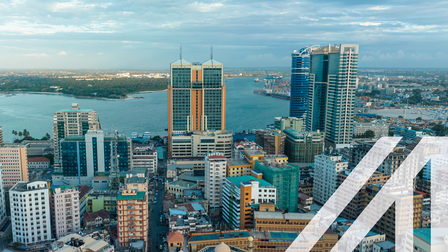 Luftaufnahme von Dar Es Salaam in Tansania: bunte Hochhäuser unter blauem leicht bewölkten Himmel, im Hintergrund erkennt man den Ozean. Über das Bild wurde ein weißes Austria A gelegt.<br />
