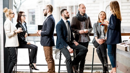 Gruppe von Personen in Businesskleidung steht und sitzt in einer hellen und modernen Cafeteria und unterhält sich