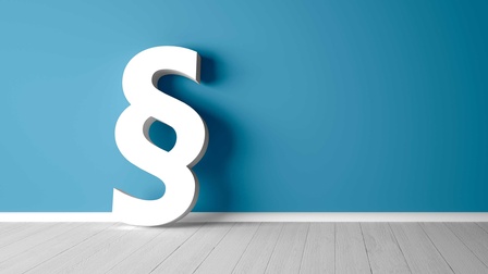 Ein großes Paragraphensymbol lehnt vor einer blauen Wand