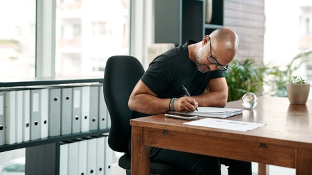 ein Mann in seinem Büro füllt Papiere auf seinem Schreibtisch aus