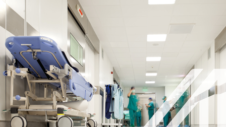 Weißer Korridor eines Krankenhauses mit Krankenhausbett und medizinischem Personal in grüner OP-Kleidung