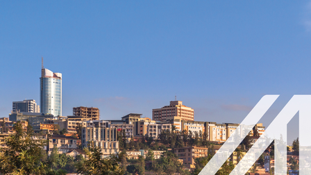 Stadtansicht von Kigali: Im Vordergrund Bäume, im Hintergrund mehrstöckige Häuser auf Hügel gelegen, darüber blauer Himmel