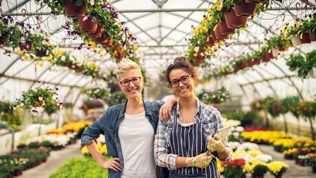 Zwei Personen mit Brillen stehen freudig in einem Gewächshaus voller Pflanzen beisammen 