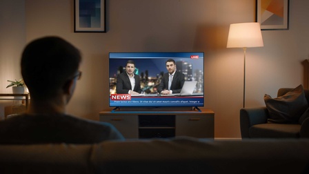 Eine Person sitzt auf einem Sofa und schaut Fernsehen