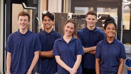 Porträt von fünf Personen. Jede Person trägt ein blaues Oberteil. Die Personen stehen in zwei Reihen. Alle haben die Mundwinkel leicht nach oben gezogen