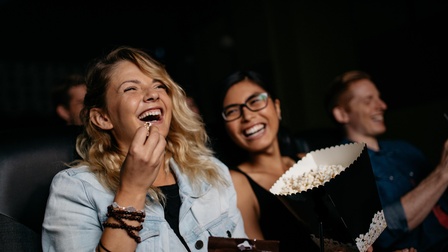 zwei Frauen sitzen im Kino, essen Popcorn und lachen