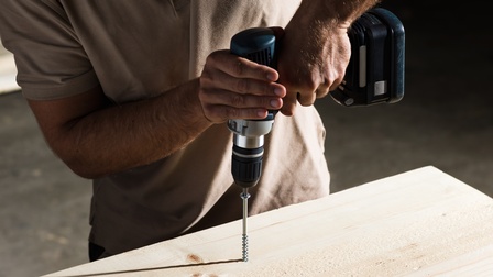 Eine Person schraubt eine Tenz-Schraube mit einem Akkuschrauber in Holz