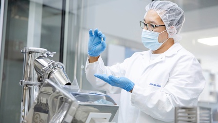 Ein Mitarbeiter in medizinisch-steriler Kleidung bei der Begutachtung einer frisch abgefüllten Kapsel