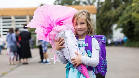 Junges Mädchen mit einer Schultüte lächelnd vor einer Schule