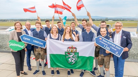 Verabschiedung der Skillsteilnehmer. Sie feier und lassen flaggen wehen, im Hintergrund ein Flugzeug, auch WKO Präsident Josef Herk und Wirtschaftslandesrätin Barbara Eibinger-Miedl sind am Bild