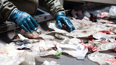 Mensch der mit Handschuhen Müll auf Förderband sortiert