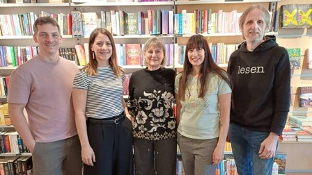 Fünf Personen stehen nebeneinander vor gefüllten Bücherregalen in einer Buchhandlung und blicken in Richtung Kamera.