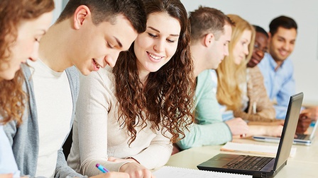 Seitliche Aufnahme von sieben Jugendlichen, die nebeneinander an Tischen sitzen. Vor zwei steht ein aufgeklappter Laptop. Eine Person notiert etwas auf einem Notizbuch