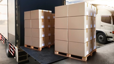 Pakete stehen auf Europaletten und werden in einen LKW geladen