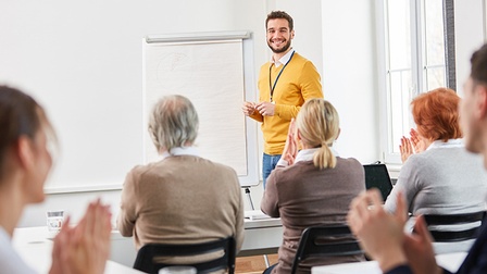 Person steht vor Flipchart und lächelt applaudierendes Publikum an