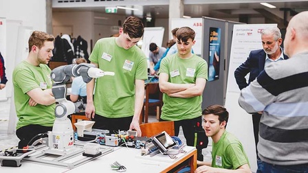 Personen unterschiedlichen Alters rund um einen Roboterarm.