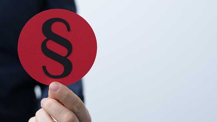 Person hält runden roten Sticker mit schwarzem Paragraph Zeichen in der Hand.