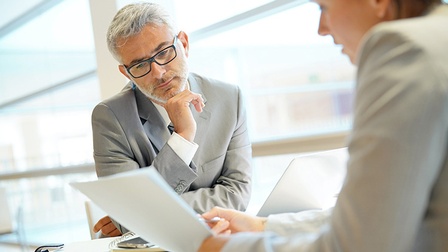 Zwei Personen sitzen an Tisch und blicken auf Dokument