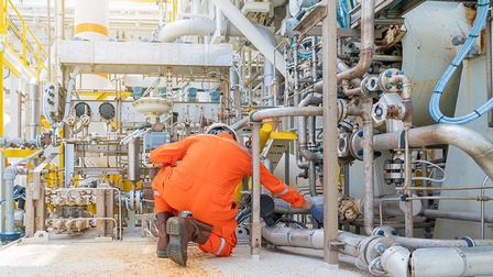 Person in orangem Schutzanzug in Rückenansicht kontrolliert auf Boden kniend Leitungen