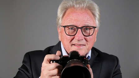 Gerhard Brischnik mit schwarzer Brille hält eine Kamera in der Hand