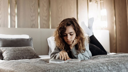 Teenager-Mädchen liegt auf dem Bett, liest ein Buch