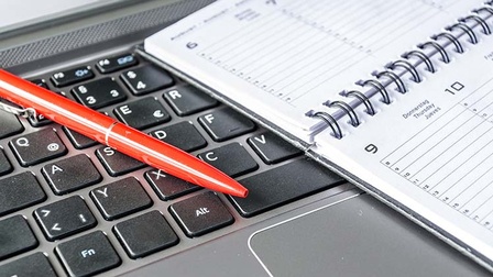 Detailansicht eines roten Kugelschreibers auf Tastatur liegend, daneben Kalender platziert