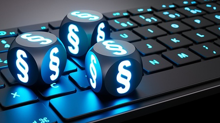 Nahaufnahme einer Computertastatur auf grauem Untergrund stehend. Auf der Tastatur liegen drei Würfel. Auf jeder Seite eines jeden Würfels ist ein leuchtendes Paragraph-Symbol