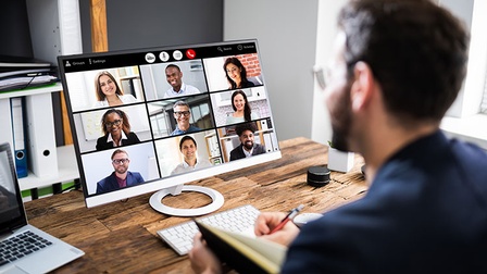 Person vor Computer sitzend, mehrere lächelnde Personen am Bildschirm