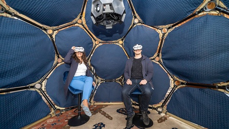 Zwei Personen, links Fjolla Holzleitner, rechts Fabian Kleindienst, sitzen mit Virtual-Reality-Brille im dunkelblauen, futuristisch aussehenden Dome.