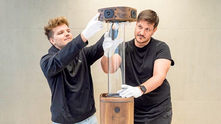 Dominic Berner (links) und René Nagl (rechts) hantieren mit ihrem Produkt: Eine Glasröhre auf einem Gerät im Holz-Look.