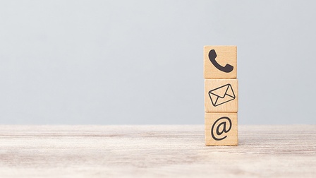 Drei Holzwürfel aufeinander gestapelt mit Kontaktsymbolen Telefonhörer, Briefumschlag und @