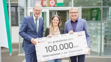 WKO Steiermark-Direktor Karl-Heinz Dernoscheg (l.) und Präsident Josef Herk (r.) gratulierten dem 100.000. Mitglied Katharina Dingsleder. Sie halten eine große Glückwunschkarte in der Hand und stehen vor der Regionalstelle Südsteiermark.