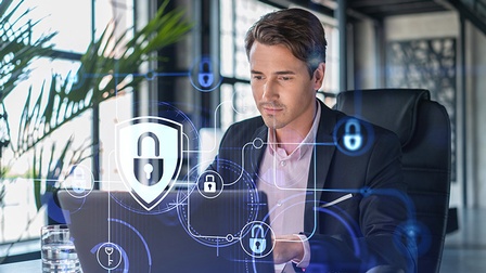 Porträtaufnahme einer Person, die auf einen Laptop blickt. Die Kulisse ist ein steriles Büro. Im Vordergrund sieht man Schloss-Symbole als Grafiken, die Sicherheit symbolisieren.