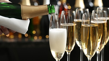 Detailansicht mehrerer Sektflöten, Sektflasche mit Serviette gehalten schenkt ein Glas perlenden Schaumweins ein