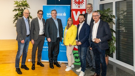 Sieben Personen stehen nebeneinander in einem Veranstaltungsraum der WK-Bezirksstelle Schwaz und blicken in die Kamera. Hinter ihnen sind ein Banner der Sparkasse Schwaz sowie ein WKO-Aufsteller zu sehen.