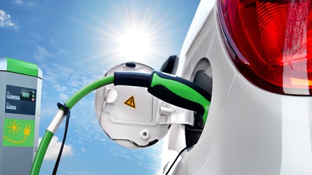 Weißes Elektroauto beim Tanken, im Hintergrund blauer Himmel und Sonnenschein