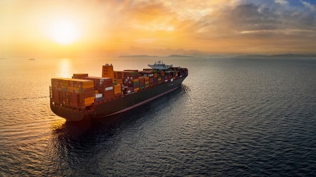Ein Frachtschiff mit vielen Container fährt auf dem Meer. Im Hintergrund ist Festland