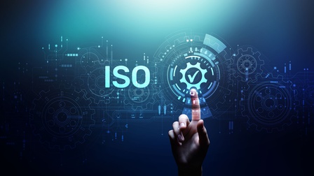 Vektor-Illustration eines bläulichen Hintergrunds, auf dem ISO steht. Um diese Buchstaben sind mehrere Zahnräder gelegt. Direkt rechts daneben ist ein Kreis mit einem Haken, auf den der rechte Zeigefinger einer Person deutet