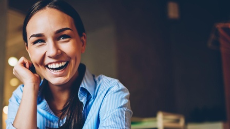 Lachende Person in blaugestreiftem Hemd stützt einen Arm an die Wange, der andere Arm am Tisch abgestützt mit iWatch am Handgelenk