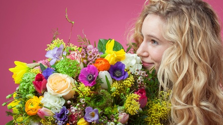 Blonde Frau riecht an Blumenstrauß und lächelt