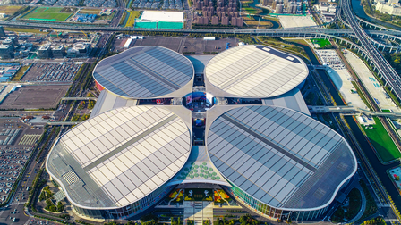 Aufnahme einer großen Halle aus der Vogelperspektive mit vier Gebäudeteilen. Um das Gebäude sind mehrere Parkplätze