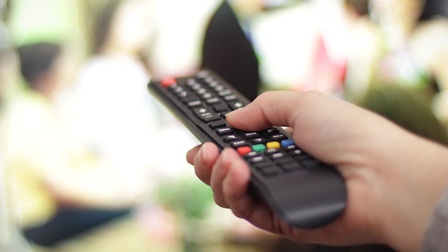 Nahaufnahme der rechten Hand einer Person, die eine Fernbedienung horizontal hält