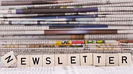 Newsletter: die einzelnen Buchstaben auf Holzwürfel und im Hintergrund ein Zeitungsstapel