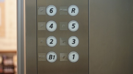 Nahaufnahme von Stockwerkknöpfen in einem Aufzug, daneben ist jeweils die Brailleschrift angegeben