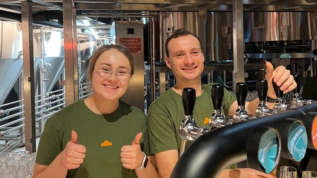Frau und Mann hinter einer Bar vor einer Zapfanlage, sie recken die Daumen nach oben