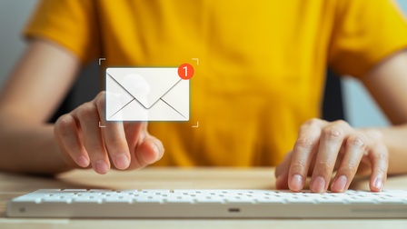 Frontale Aufnahme der Hände einer Person, die auf einer Computertastatur tippt. Über der Tastatur ist ein Icon eines Briefumschlags. An der rechten oberen Ecke des Briefumschlags ist eine weiße eins in einem roten Kreis