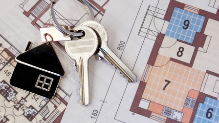 Nahaufnahme eines Plans einer Wohnung oder eines Hauses, auf dem ein Schlüsselbund mit einem Schlüsselanhänger in Form eines Hauses liegt.