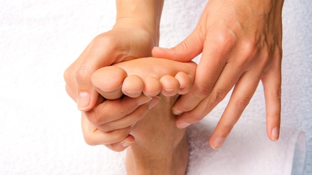 Nahaufnahme eines Fußes einer Person aus der Vogelperspektive, der auf einer Massageliege auf einem Handtuch liegt und von einer anderen Person massiert wird