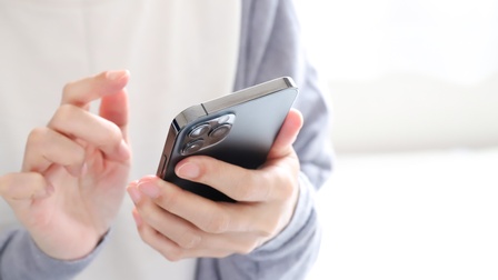 Man sieht die Hand eines Mannes, die ein Handy hält