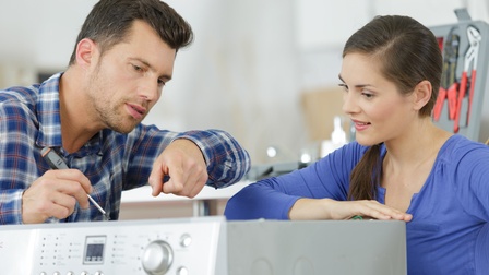 Mann und Frau überprüfen eine kaputte Waschmaschine.